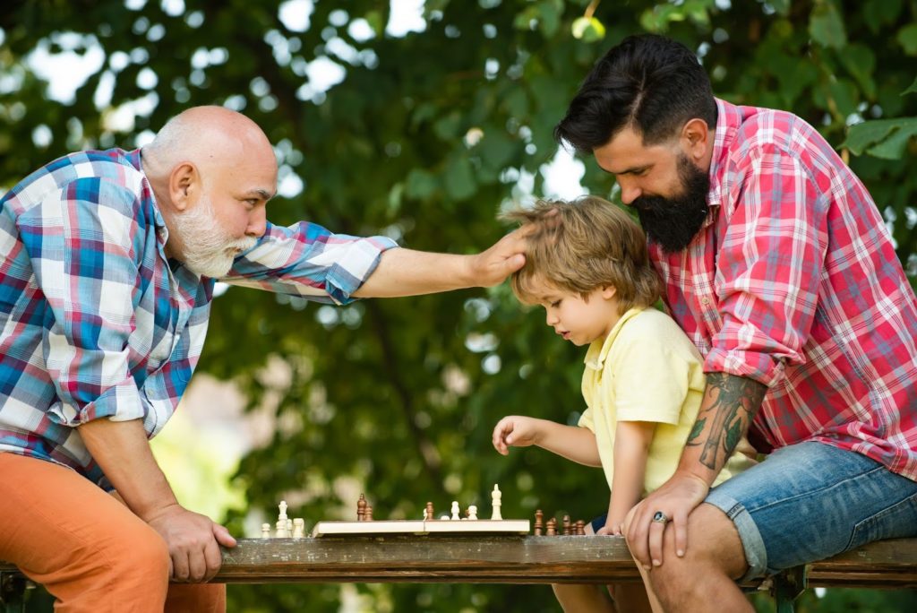 A grandfather, father, and son playing chess together.