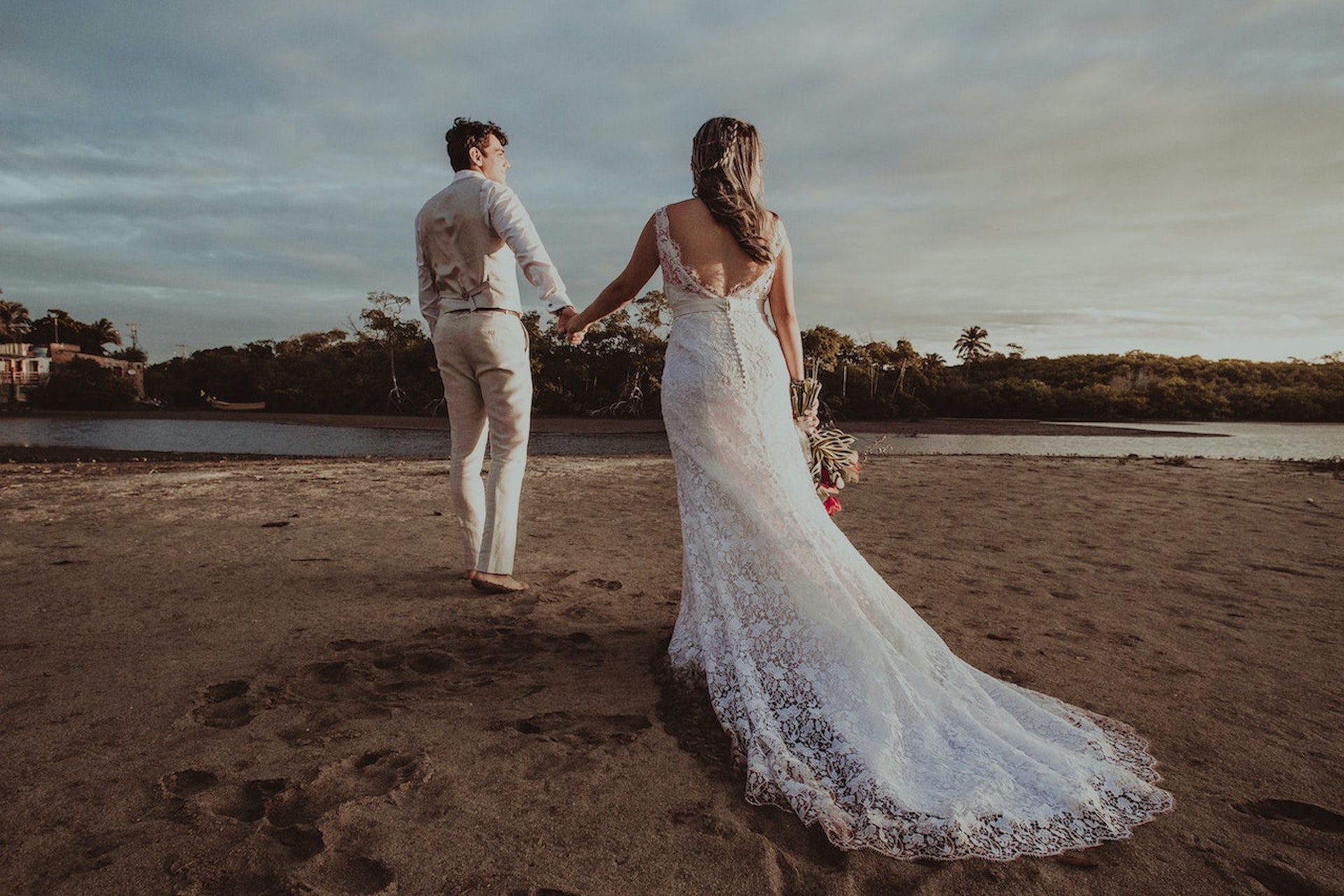 groom and bride in wedding clothes holding hands on a beach for a Bella Mansions blog on selecting a summer wedding venue